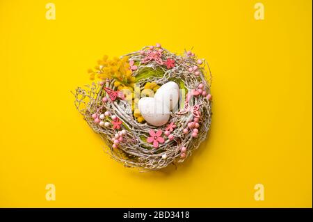 Easter eggs in a basket of flowers and branches on a yellow background. Happy Easter card with copy space for text. Minimal style Stock Photo