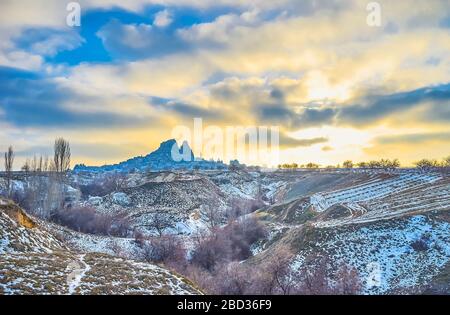 The colorful sunset over the snowy lands of Cappadocia and the silhouette of Uchisar rock castle on horizon, Turkey Stock Photo