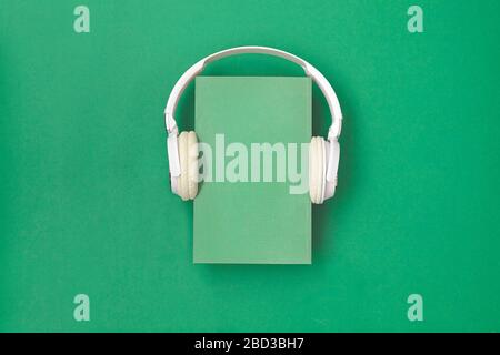 Book is white with headphones on green background. Top view. Stock Photo