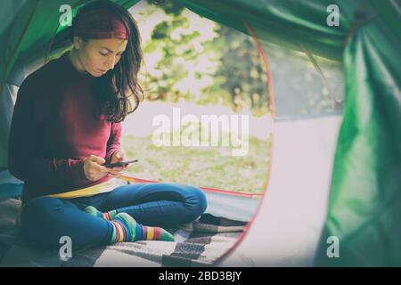 European woman in a tent overlooking the forest  holds a telephone in her hands. A modern holiday with devices and the Internet, to be always in touch Stock Photo