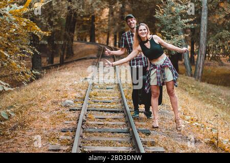 A young couple of lovers missed the train. Hitchhikers on the rails in the autumn forest waiting for the next train. Stock Photo