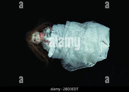 A dark, scary edit of an old doll wrapped in a white net curtain on a black background Stock Photo