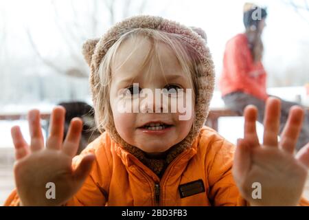 young girl with animal hoodie looks at camera, pushes against window Stock Photo