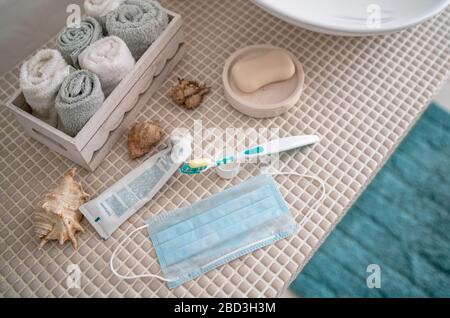 Open toothpaste, a toothbrush, and a medical mask that has been removed from your face are lying on the table in front of the washbasin in the bathroo Stock Photo