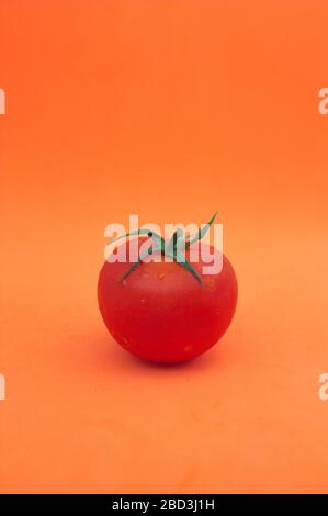 A ripe tomato with its stem and natural leaves on an orange background and space for text. Stock Photo