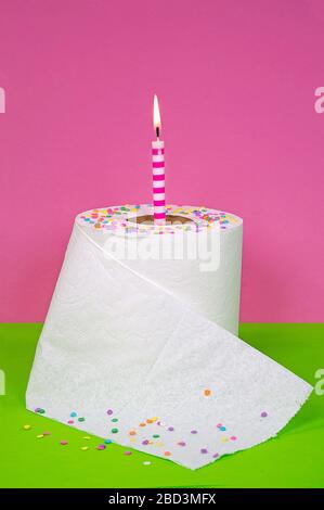 candy confetti and birthday candle in white toilet paper roll on green and pink background Stock Photo