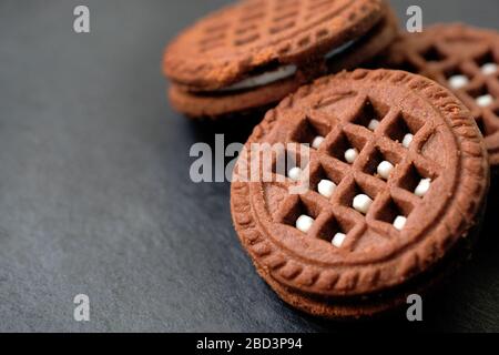 Close-up round chocolate chip cookies with white filling. Chocolate friable cookies on a black background. A delicious dessert for tea. Stock Photo