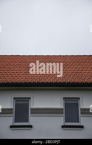 Windows on side of a house with orange roof and gray sky Stock Photo