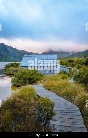 Iconic view along the wooden boardwalk leading to the wooden boathouse on Dove Lake, in the Cradle Mountain National Park in Tasmania, Australia. Stock Photo