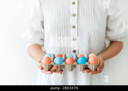 Woman in rustic linen white dress holding carton box with painted red and blue eggs for Easter close up. Paschal concept. Stock Photo
