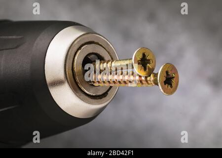 Self-tapping screws are inserted into the power tool with the reverse side. Concept on the misuse of a screwdriver Stock Photo