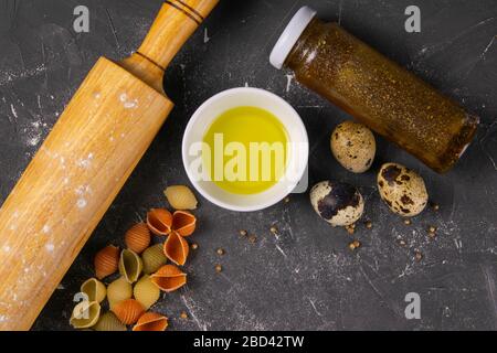 Pasta Conchiglie Rigate, mix of colorful uncooked shells with rocking for dough, olive oil, spices and quail eggs. Textured Italian food background Stock Photo