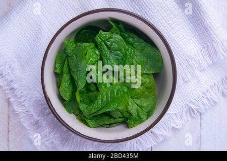 Spinach in a plate on a white towel on wooden background. Top views, close-up Stock Photo