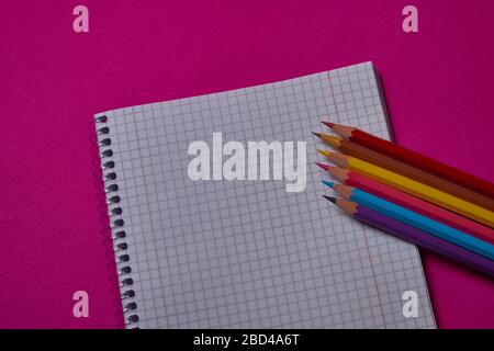 Multi colored crayons and binder notepad at magenta background with copy space. Stock Photo