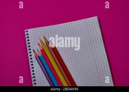 Multi colored crayons and binder notepad at magenta background with copy space. Stock Photo