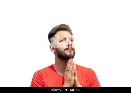 Close up portrait of handsome bearded young man looking up with hope, keeping palms together as praying isolated on white. Calm and focused on some th Stock Photo