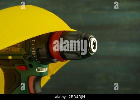 Cordless drill under yellow hardhat on a workbench, blurred in background. Construction tools and work equipment in close-up with copy space Stock Photo