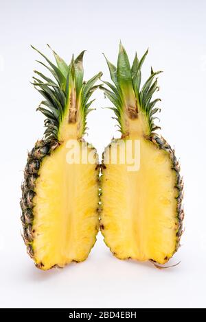 pineapple cut in half isolated in front of a white background. The yellow core of the fruit is juicy and colorfull with green leaves Stock Photo