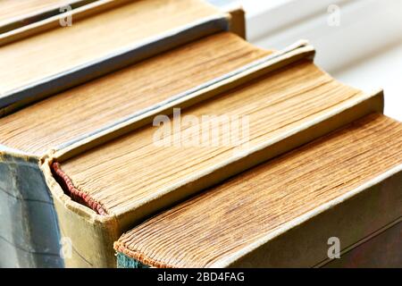 Old books in a row. Monochrome coloured weathered, aged, stained and torn antique books with red white headband. Closeup shot with selective focus. Stock Photo