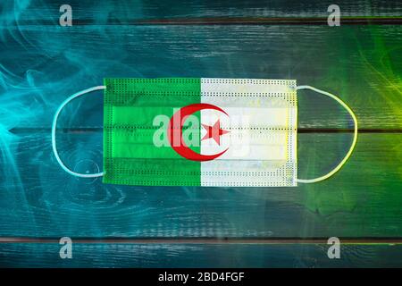 Medical mask for protection against airborne diseases, painted in the national flag of Algeria  on a black background in blue-green smoke. Medical pro Stock Photo