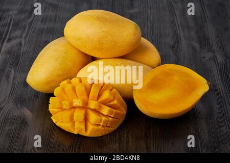 Four whole mango fruits on wooden table and cut into slices. Large juicy bright ripe yellow fruits Stock Photo