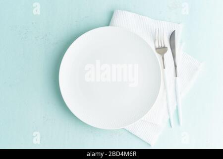 Clean empty white plate, fork and knife on green blue turquoise stone table, copy space, mock up Stock Photo
