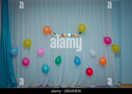 There are multi-colored balloons on the curtain . Colorfull Happy Birthday text on white curtain background . Stock Photo