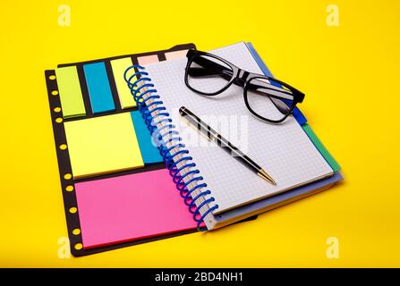 Office background. Copybook, glasses, pen, office supplies and stickers on yellow background. Top view, copy space, flat lay Stock Photo
