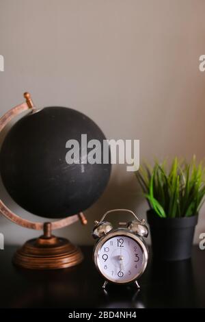 Black globe and clock standing on table near houseplant. Stock Photo
