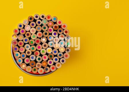 Colour pencils in metal holder on yellow background. School supplies. Back to school. Top view, free copy space for text. Macro with extremely shallow Stock Photo