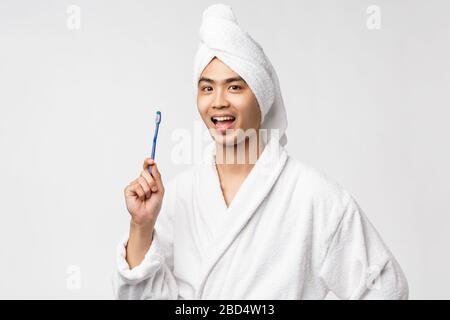 Beauty, spa and leisure concept. Cheerful handsome asian man in bathrobe and bath towel, showing toothbrush and smiling upbeat, washing-up at morning Stock Photo