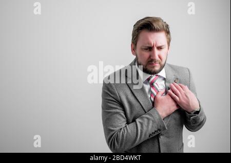 Portrait of business man wearing business clothes with his hand on his chest suffering from acute pain isolated on grey background with copy space adv Stock Photo