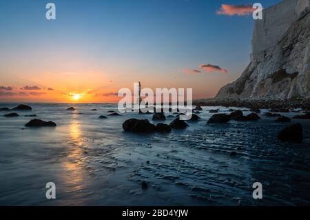 Down on the beach at low at Beachy head near eastbourne with the sun setting behind the lighthouse Stock Photo