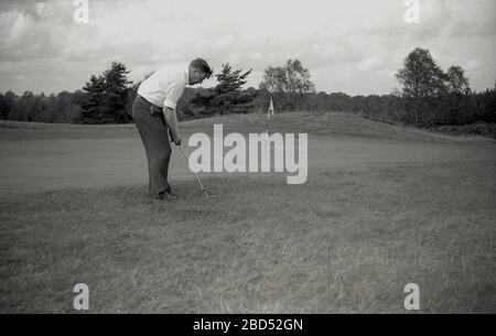 1960s, historical, Outside on an inland golf course, an adult male golfer chipping towards the flag at the edge or fringe of a putting green, England, UK. Stock Photo