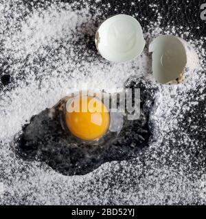 One quail egg broken into flour on black background Stock Photo