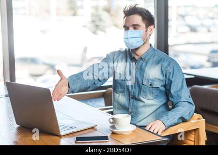 Welcome! Portrait of satisfied businessman with surgical medical mask sitting and greeting a worker through a webcam and showing handshake gesture wit Stock Photo
