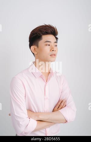 Smiling Asian man wearig pink shirt standing with hands folded over white background Stock Photo