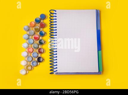 Colored paints for drawing. Notebook on a yellow background. Top view school supplies with blank notepad. Back to school Stock Photo