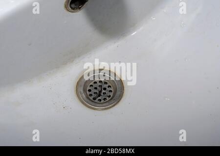 Dirty ceramic sink in a motel. A detailed shot of a shell with dirt, sand and hair. Top view at an angle. Selective focus. Close-up Stock Photo