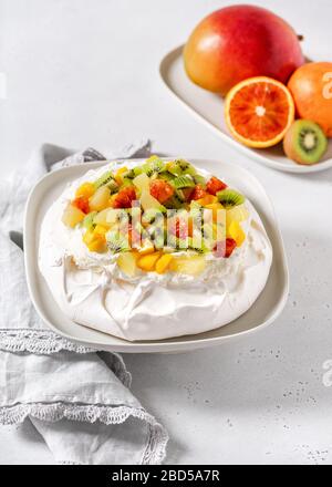 Tropical Pavlova meringue cake with kiwi, mango, pineapple, blood orange slices and whipped cream. Delicious summer dessert. Selective focus. Stock Photo