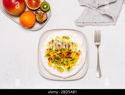 Pavlova meringue cake with kiwi, mango, pineapple, blood orange slices and whipped cream over gray stone background. Top view. Copy space. Stock Photo