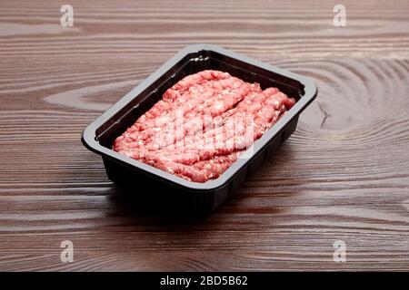 Ground beef in a black plastic tray on wooden table. Uncooked mincemeat. Forcemeat, fresh raw minced meat Stock Photo