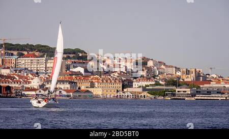A chartered tour yacht on the Tagus River with a backdrop of urban Lisbon, Portugal, basking in the dusky late afternoon sun. Stock Photo