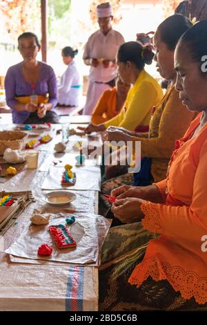 Vertical portrait of women and a holyman making religious decorations at a temple in Bali, Indonesia. Stock Photo