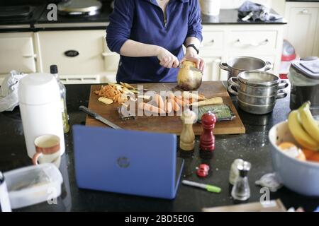 Mother preparing and cooking family dinner meals in kitchen whilst working from home during self-isolation - 2020 COVID-19 coronavirus pandemic Stock Photo