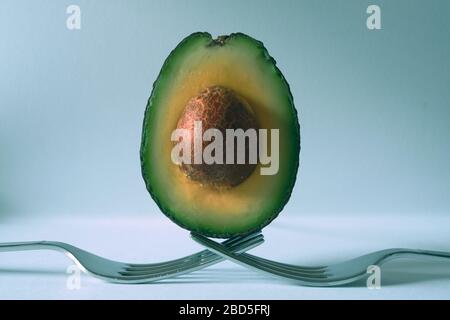 Avocado half balanced on forks with light blue background Stock Photo