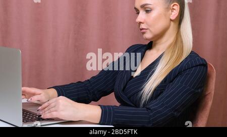 Serious female secretary typing on a laptop sitting at a table at his workplace. Stock Photo
