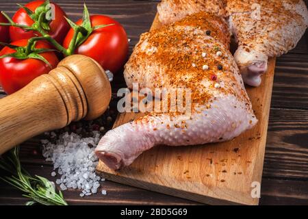 Raw chicken legs on a cutting board on a wooden table. Marinated chicken leg with spices and tomatoes Stock Photo