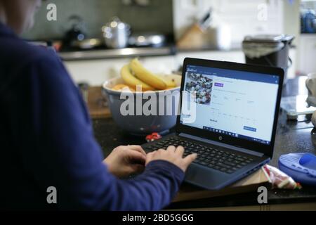 Mother prepares family dinner at home whilst working on laptop in kitchen during self-isolation during the 2020 COVID-19 coronavirus pandemic Stock Photo