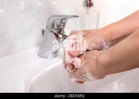 Woman using soap and hot water to wash her hands over a washbasin in a bathroom. Coronavirus pandemic prevention. Stock Photo
